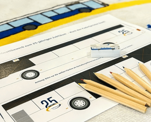Mehrere Stifte und ein Radiergummi liegen auf einer Malvorlage. Die Malvorlage zeigt einen Bus von seinen beiden Längsseiten. Als Untergrund dient ein Teppich auf dem das 25 Jahre PaderSprinter-Logo aufgestickt ist.